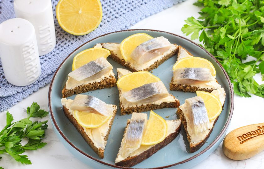 1. Этап. Канапе с селедкой и лимоном: Четверть лимона нарежьте ломтиками и удалите косточки. Выложите на канапе.