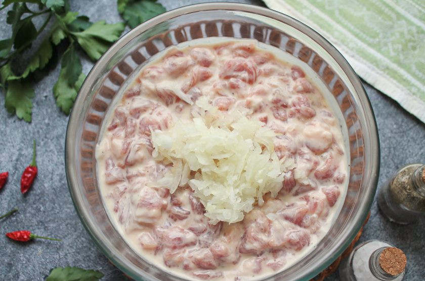 1. Этап. Мясо по-албански из свинины: Натрите репчатый лук на крупной терке и выложите в массу, перемешайте.