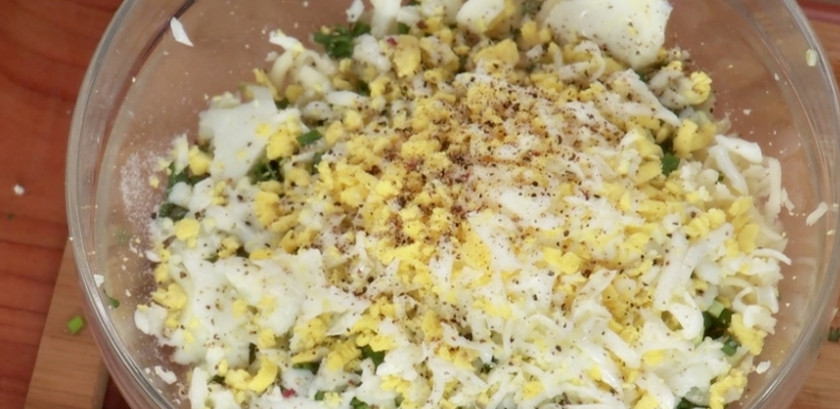 1. Этап. Осетинский пирог с сыром сулугуни: Пока тесто находится на расстойке, приготовьте начинку. Для этого отварите яйца вкрутую, очистите их и нарежьте как можно мельче. Зеленый лук вымойте и нашинкуйте. Сулугуни натрите на крупной терке. Все ингредиенты отправьте в миску, поперчите и тщательно перемешайте.