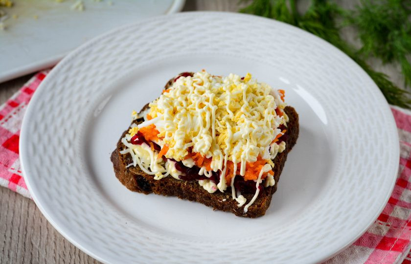 1. Этап. Селедка под шубой на хлебе: Присыпьте слоем из тертых яиц и снова нанесите сеточку из майонеза.