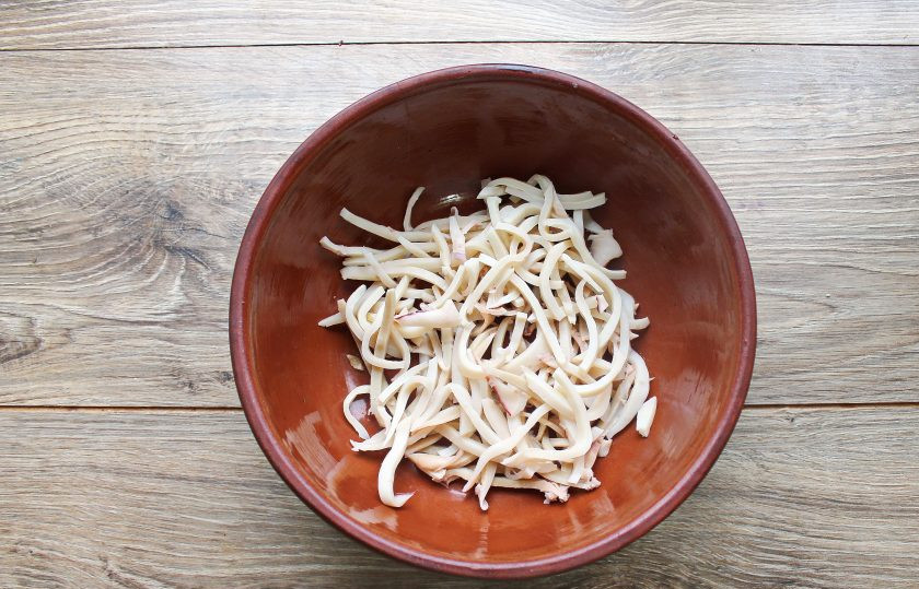 1. Этап. Салат с кальмарами, креветками и кукурузой: Кальмара очистите от верхней оболочки и сполосните. В кастрюлю налейте воду и доведите до кипения. Опустите кальмары, доведите до кипения, варите в течение 2 минут после закипания. Слейте отвар, и остудите кальмары. Порежьте их соломкой и выложите в миску.