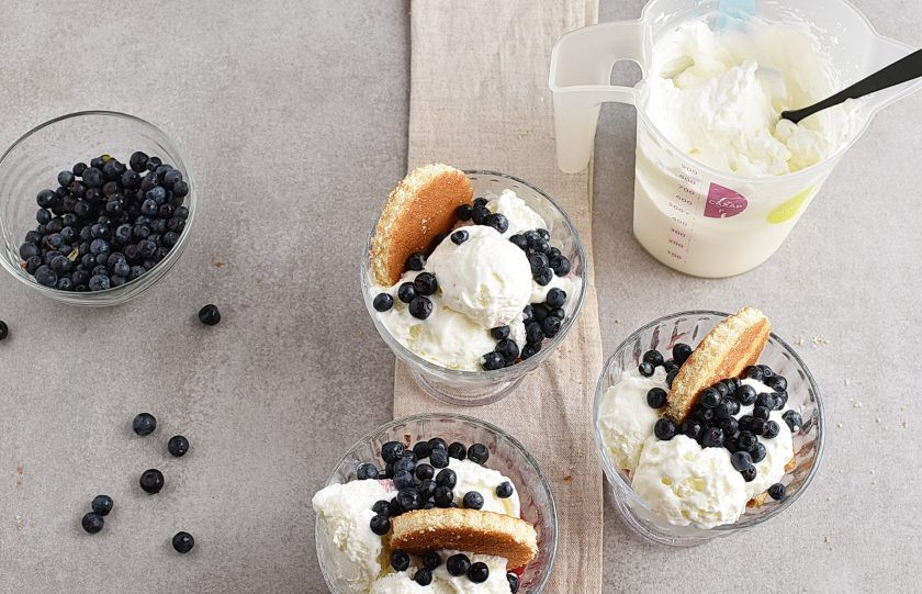 1. Этап. Десерт из мороженого: Разложите мороженое с помощью специальной ложки шариками по креманкам. Добавьте с одного бока взбитые сливки. С другой стороны воткните по кружочку бисквита. Щедро присыпьте черникой и при желании украсьте меренгой или шоколадом.