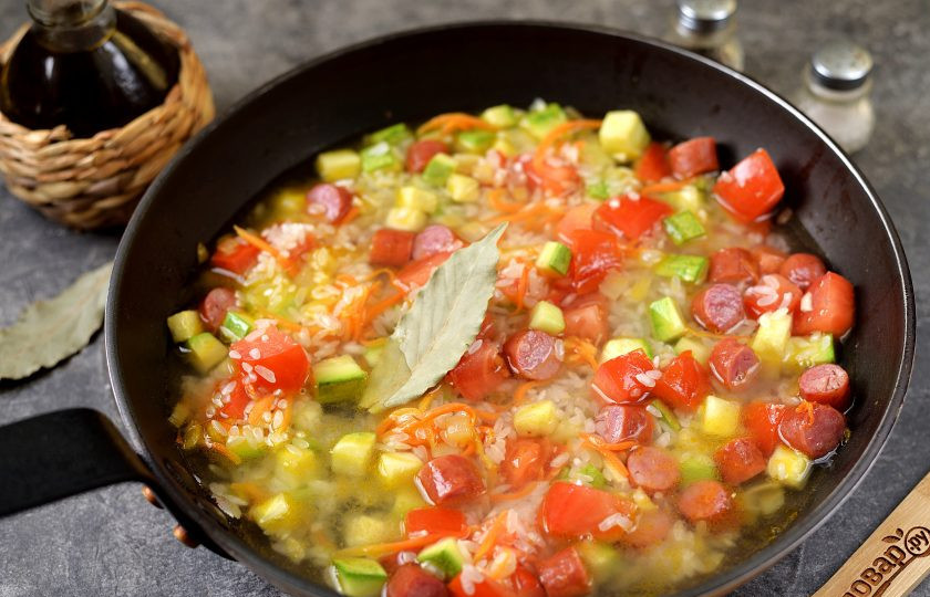 1. Этап. Рис с колбасками и овощами: Влейте теплой воды из чайника столько, чтобы она слегка покрывала содержимое сковороды. Посолите и поперчите по вкусу, добавьте лавровый лист. Как только вода закипит, накройте крышкой сковороду, сделайте огонь тихим и тушите блюдо 18-20 минут. Спустя время выключите плиту, оставьте рис под крышкой еще минут на 15.