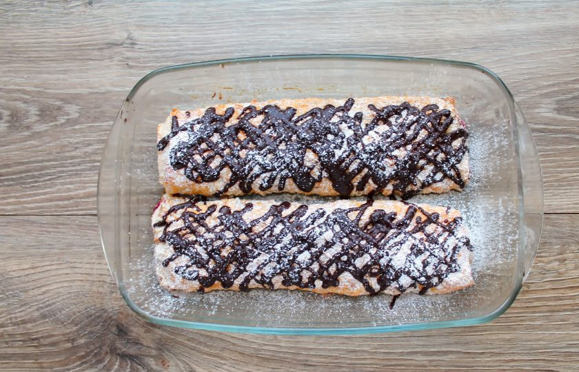 1. Этап. Рулет из лаваша с творогом и вишней: Достаньте рулет из духовки и дайте ему остыть. Шоколад поломайте и растопите на водяной бане и нанесите на поверхность рулета. Затем посыпьте его сахарной пудрой. Дайте шоколаду застыть, порежьте и подавайте к столу.