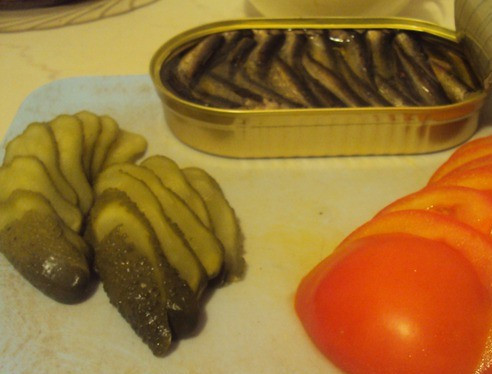 1. Этап. Бутерброды со шпротами и помидорами: Помидоры промойте и порежьте колечками. Огурчики порежьте тонкими ломтиками.