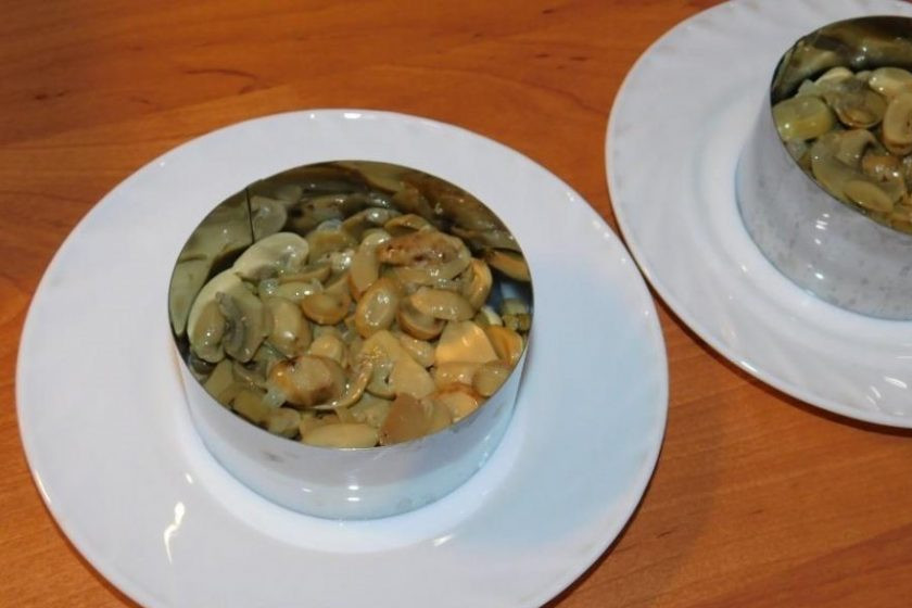 1. Этап. Слоеный салат с курицей, грибами и грецкими орехами: Выложите обжаренные грибы первым слоем салата. Смажьте майонезом.