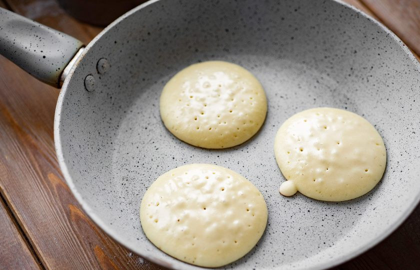 1. Этап. Панкейки на йогурте пышные: Сухую сковороду с качественным антипригарным покрытием разогрейте на умеренном огне и выкладывайте тесто по одной столовой ложке, формируя панкейки. Обжаривайте с одной стороны до появления пузырьков на поверхности теста, после чего панкейки переверните на другую сторону лопаткой.