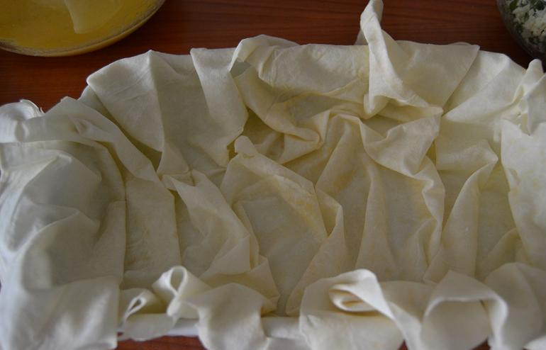 1. Этап. Берек с сыром: Противень или большую форму для запекания смазываем растительным маслом. Выкладываем на дно первый пласт теста, собираем его складками по дну и оставляем длинные края.