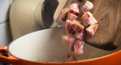 1. Этап. Свинина с фасолью и помидорами: 3. Поставьте толстостенную большую кастрюлю на огонь. Нам в нее надо будет вместить все ингредиенты, включая пол-литра бульона. На масле обжарьте до золотистого цвета обваленную в муке свинину. Затем выберите кусочки на блюдо. Бекон нарежьте кубиками и отправляйте в ту же кастрюлю. Туда же выложите лук и чеснок, обжарьте, помешивая, до золотисто-коричневого цвета.