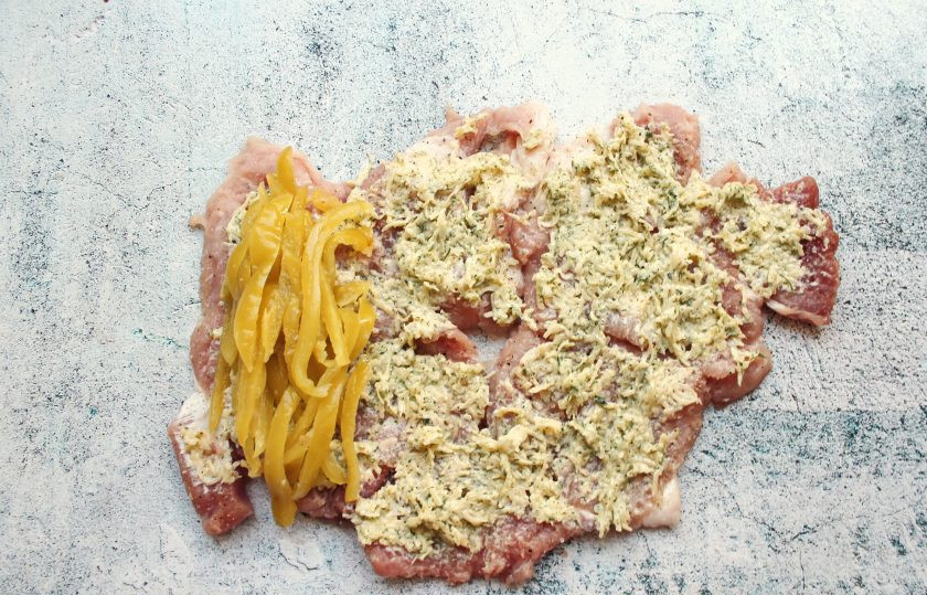 1. Этап. Свинина фаршированная маринованным перцем: Нанесите сырную массу на всю поверхность свинины. Маринованный перец порежьте соломкой и выложите на один край. Сверните свинину, начиная со стороны перца, в плотный рулет.