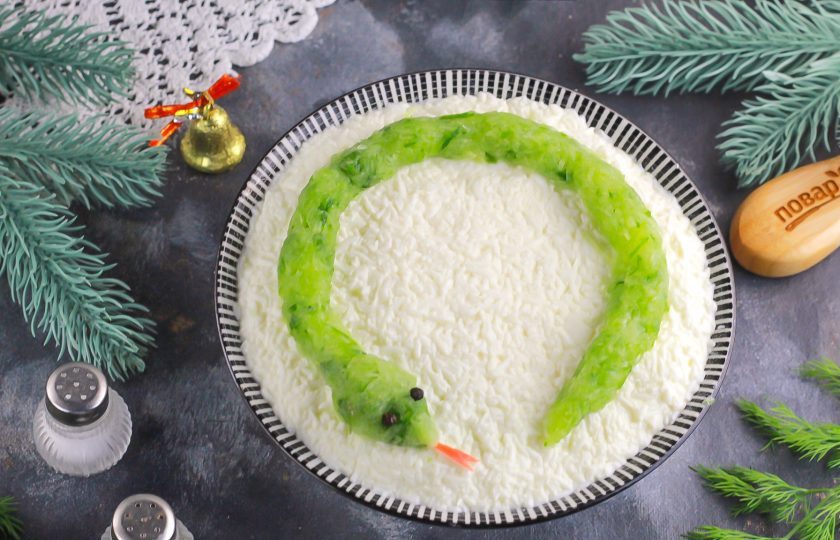 1. Этап. Крабовый салат на Новый год 2025: Огурец промойте в воде, обсушите бумажной салфеткой и срежьте хвостики. Натрите на терке с мелкими ячейками и оставьте нарезку на 5 минут. Затем тщательно отожмите. Если этого не сделать, то украшение из массы 