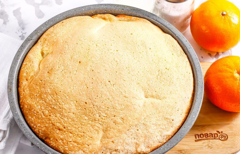 1. Этап. Бисквит с мандаринами: Как только бисквит хорошенько подрумянится — он готов, можете выключить нагрев. Переверните его прямо в форме и поместите на две чашки для остывания. Если не перевернуть бисквит дном вверх, то он осядет и опадет.