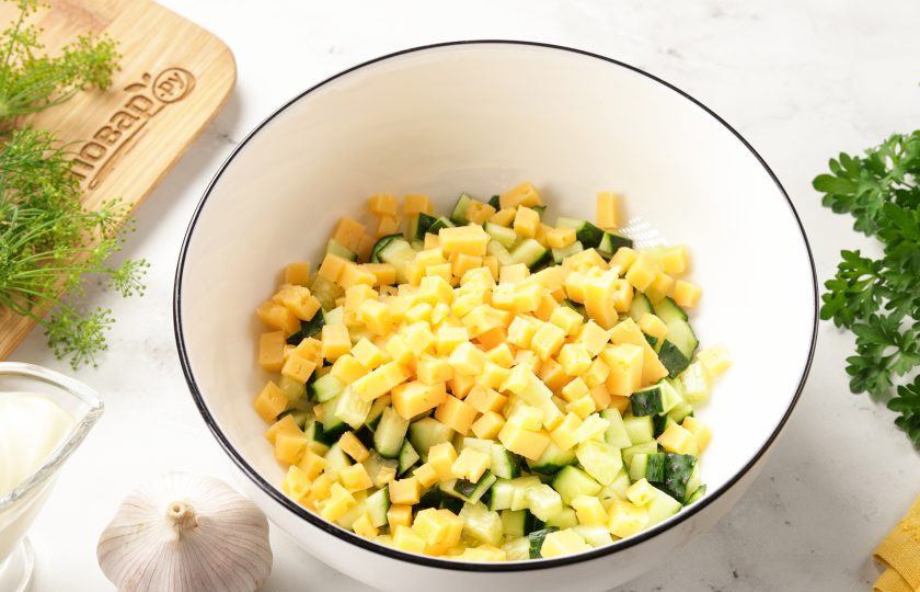 1. Этап. Салат с яйцом, сыром, кукурузой и огурцом: Добавьте нарезанный кубиками сыр.