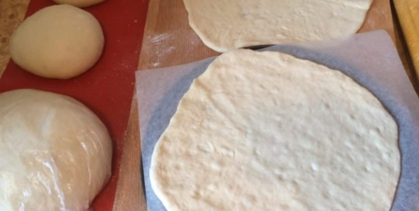 1. Этап. Булочки, политые шоколадом: Раскатайте один шарик в тонкую лепешку и выложите на круглую поверхность, размером с будущий пирог, застеленную бумагой для выпечки. Лепешку смажьте оливковым маслом и равномерно распределите несколько ложек сахара.