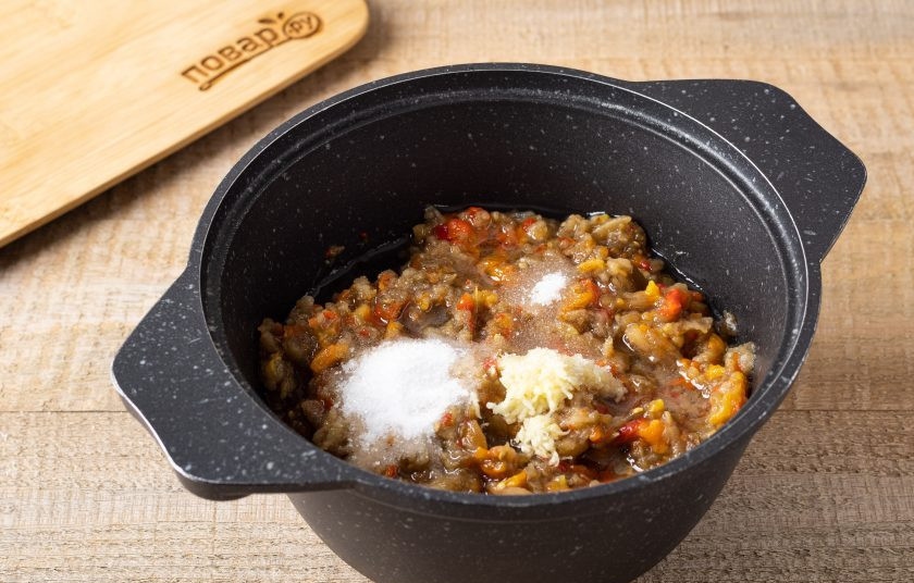 1. Этап. Айвар с баклажанами на зиму: Переложите измельчённые баклажаны и перцы в кастрюлю с толстым дном. Добавьте соль, сахар, измельчённый чеснок и влейте растительное масло. Все перемешайте. Доведите до кипения и варите после 15 минут на среднем огне. Периодически помешивайте. В конце влейте уксус и ещё раз перемешайте.