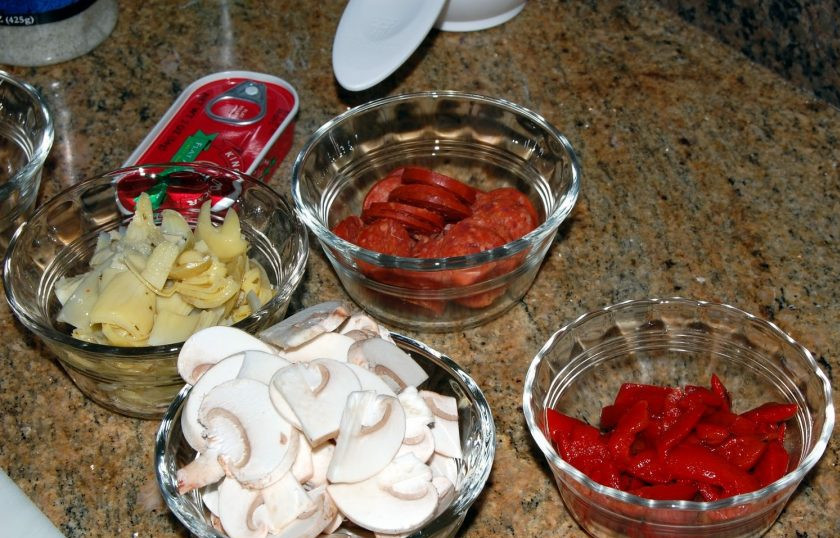 1. Этап. Сырная пицца Четыре сезона: 3. Очистите перец и нарежьте его кусочками, затем обжарьте на сковороде. Нарежьте тонко пепперони и грибы, моцареллу натрите на крупной терке, а оливки нарежьте кружочками.