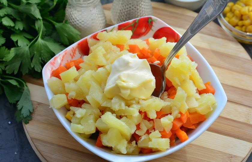 1. Этап. Салат с копченым мясом и кукурузой: Добавьте в салат нарезанные кубиками сваренные картофель и морковку. Заправьте салат майонезом, посолите и поперчите.