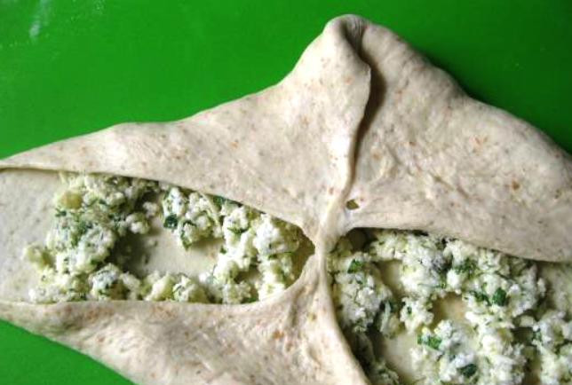 1. Этап. Осетинский пирог в духовке: Разделите подошедшее тесто на 3-4 части, раскатайте в кружки и распределите по ним начинку. Края теста соберите вокруг начинки в виде мешочка и закрепите края.