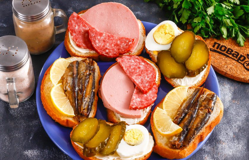1. Этап. Советские бутерброды: Извлеките шпроты из масла, слегка стряхивая рыбок от лишнего жира. Выложите на ломтики хлеба без майонеза — шпроты и так жирные. Нарежьте лимон и добавьте на бутерброды со шпротами — цитрусовый идеально дополнит рыбу по вкусу.