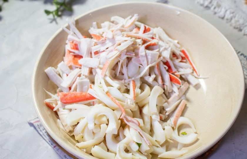 1. Этап. Салат с крабовыми палочками, кальмарами и кукурузой: Отварные кальмары нарежьте соломкой. Крабовые палочки разберите на волокна или нарежьте кубиками.