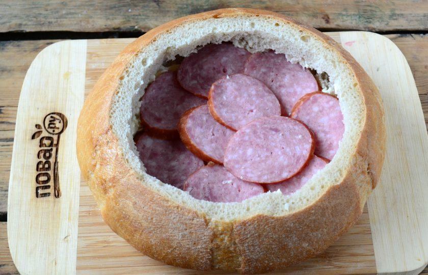 1. Этап. Гигантский мегабутер: На хлебе обрежьте верхушку толщиной примерно 2 см. Максимально выньте мякиш, освободив место для вкусной начинки. Салями нарежьте тонко, выложите на дно хлеба, устелив им все дно.