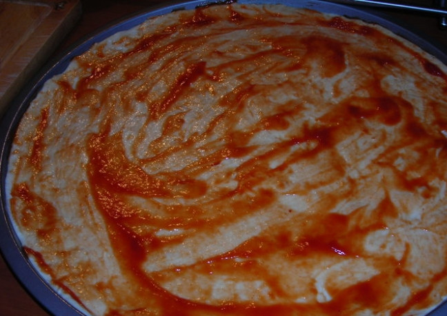 1. Этап. Пицца с сосисками и сыром: 1. В миске смешиваю теплую воду с дрожжами, затем добавляю оливковое масло, соль и пшеничную муку. Замешиваю тесто, затем перекладываю его в миску, накрываю полотенцем и оставляю на 1 час при комнатной температуре. Через час раскатываю тесто по форме и смазываю его кетчупом.