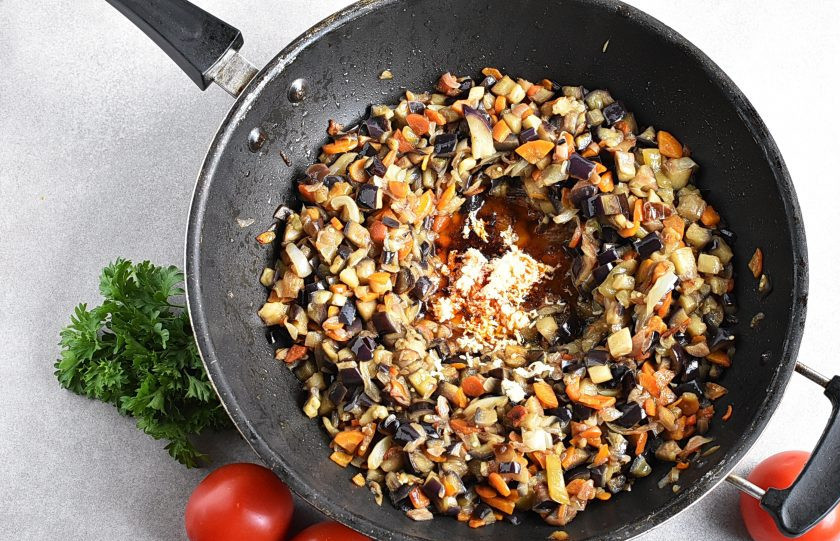 1. Этап. Икра из баклажанов на зиму: Сделайте углубление в середине жаровни. Выложите туда паприку и крупно растолченный кориандр. Выдавите чеснок. Перемешайте пряности с маслом и прогрейте пару минут, не смешивая с овощами. Затем перемешайте.