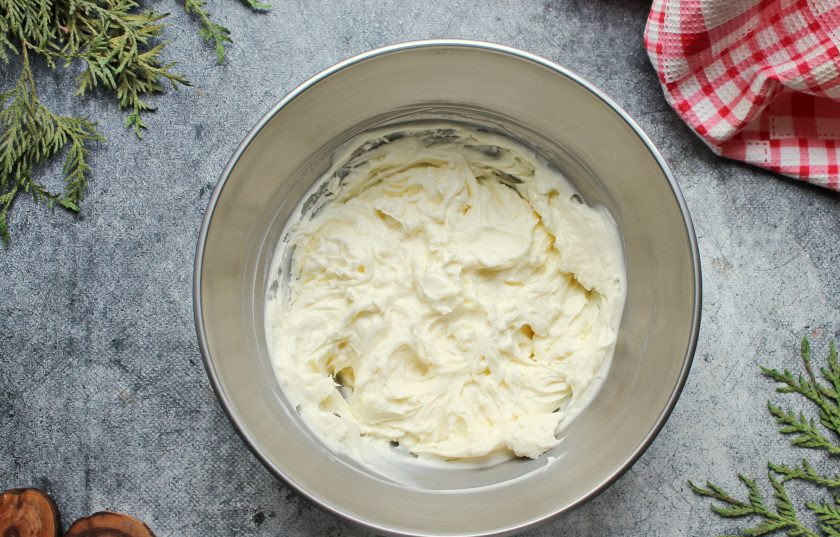 1. Этап. Муссовый торт с манго: В миску выложите сливочный сыр, добавьте сахарную пудру и влейте сливки. Все взбейте в пышный крем, выложите его на бисквит ровным слоем, оставив немного для украшения.