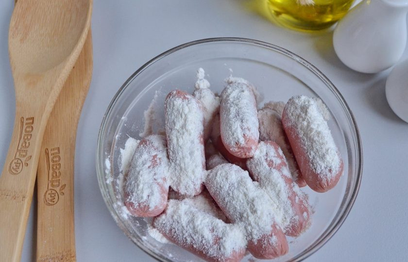 1. Этап. Мини корн-доги: С сосисок снимите оболочки, если сосиски обычные, то порежьте их на 2 части, если длинные (для хот-догов), то на 3 части. У меня сосиски мини, их резать не нужно. Обваляйте сосиски в столовой ложке муки.