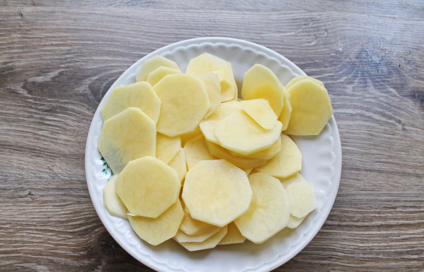 1. Этап. Гратен с беконом: Картофель почистите и порежьте тонкими кружочками. Посолите и перемешайте.