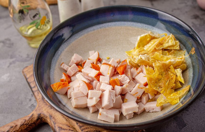 1. Этап. Салат с яичными блинчиками, копчёной курицей и кукурузой: Остывшие яичные блины разрежьте на полоски, а затем на кусочки. Добавьте их к курице.