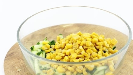 1. Этап. Салат с кальмаром и сыром: В салатницу к огурцам добавьте кукурузу без жидкости из банки.