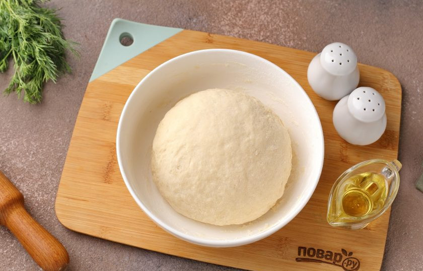 1. Этап. Вареники с адыгейским сыром и зеленью: Сначала тесто замешивайте ложкой, затем переложите на стол и продолжите замес руками. Готовое тесто не должно липнуть к рукам, оно мягкое и эластичное. Соберите его в шар, накройте полотенцем и дайте полежать 20 минут.