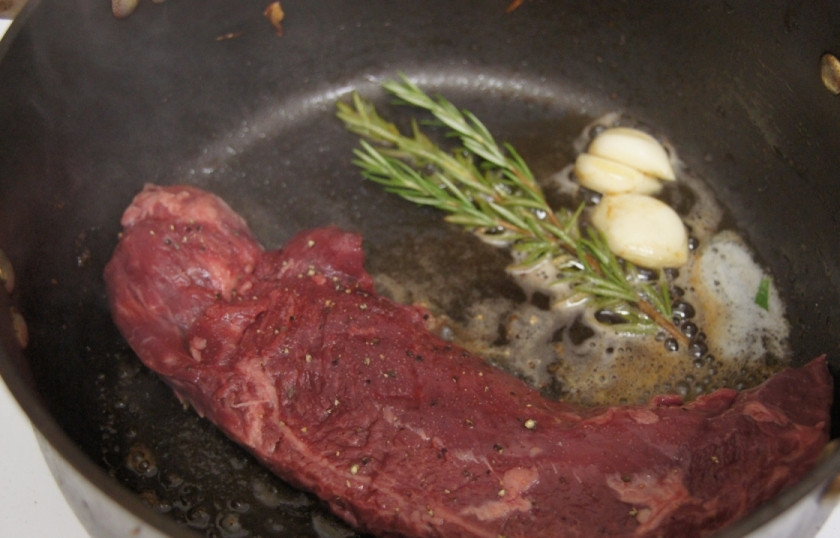 1. Этап. Стейк из говядины с грибным соусом: Отложите обжаренные грибы в отдельную чашку. На том же масле (можете немного добавить) обжарьте говяжий стейк, положите в сковороду вместе со стейком целые зубчики чеснока, веточку розмарина и зелёный лук.