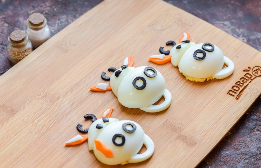 1. Этап. Фаршированные яйца на год Быка: Переверните яйца начинкой вниз, выложите на тарелку или доску, которую будете использовать для подачи закусок. Украсьте яйца маслинами, морковью, оставшимся белком, как показано на фото.