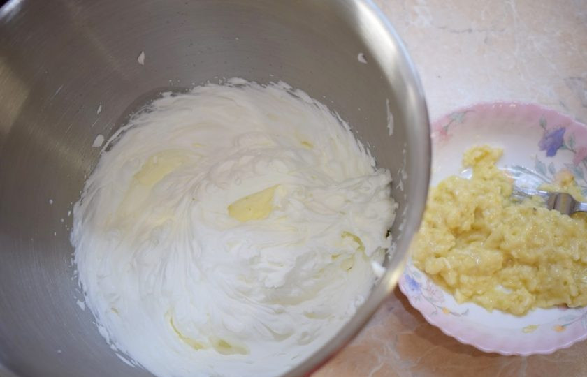 1. Этап. Банановый торт со сметанным кремом: Взбейте сметану с сахарной пудрой в пышный крем. Бананы разомните вилкой в пюре, но так, чтобы оставались небольшие кусочки. Размятый банан немного сбрызните лимонным соком, чтобы он не темнел. Смешайте венчиком пюре банана и сметанный крем.
