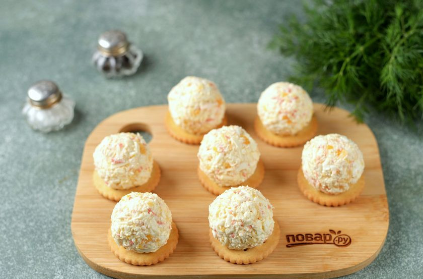 1. Этап. Новогодняя закуска Кролики на крекерах: Чайной ложкой наберите сырно-крабовую массу, скатайте из нее шарики размером с грецкий орех, выложите шарики на крекеры.