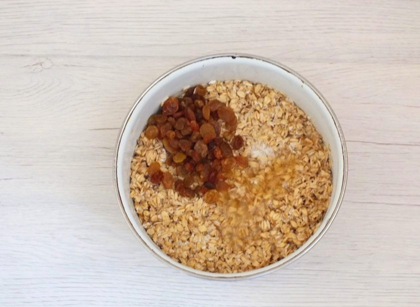 1. Этап. Творожное печенье без муки: По истечении времени к набухшей овсянке добавьте изюм, мёд, разрыхлитель. Перемешайте.