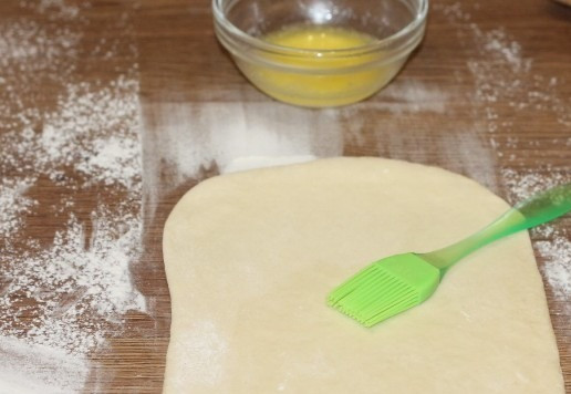 1. Этап. Слоеные пирожки с луком и картошкой: 8. Припыляем столешницу мукой и раскатываем каждую часть теста в пласт, толщиной 3 мм. Смазываем пласт теста растопленным сливочным маслом.