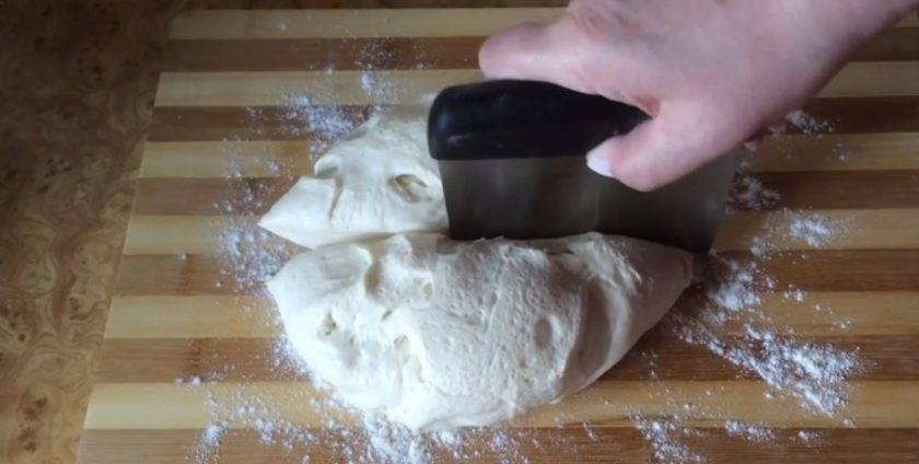 1. Этап. Французский багет на закваске: 5. Рабочую поверхность слегка присыпьте мукой, выложите тесто и разделите на две части. Каждую часть теста округлите, положите швом вверх и накройте крышкой. Оставьте на 15-20 минут, после чего аккуратно растяните тесто в лепешку.