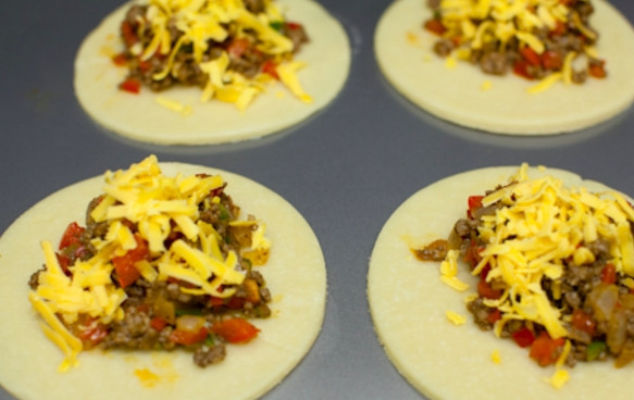 1. Этап. Духовые пирожки: Достаньте тесто и раскатайте в пласт около 3 мм толщиной, вырежьте круги диаметром 10-12 см. На каждый положите по немного начинки и присыпьте тертым сыром.