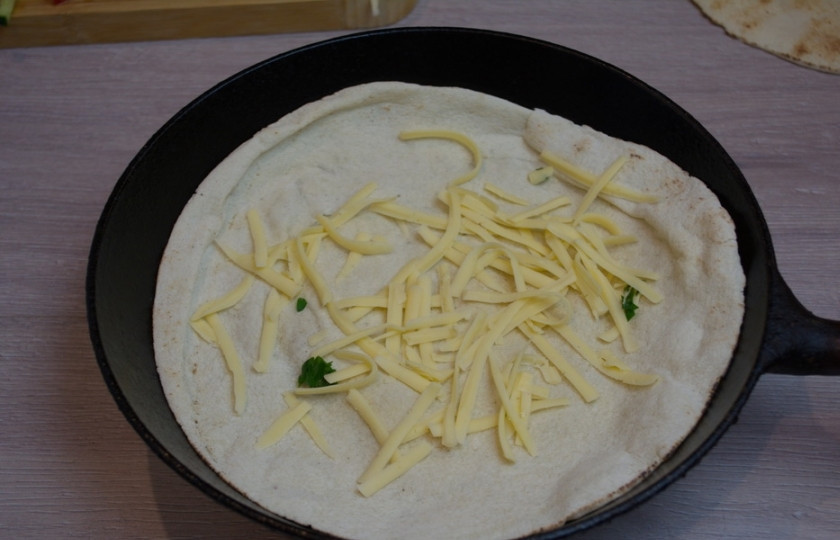 1. Этап. Кесадилья классическая: На сухую горячую сковороду выложите питу. Уменьшите сразу огонь до минимума. Посыпьте всю питу тертым сыром. Мысленно поделите питу на 2 части.