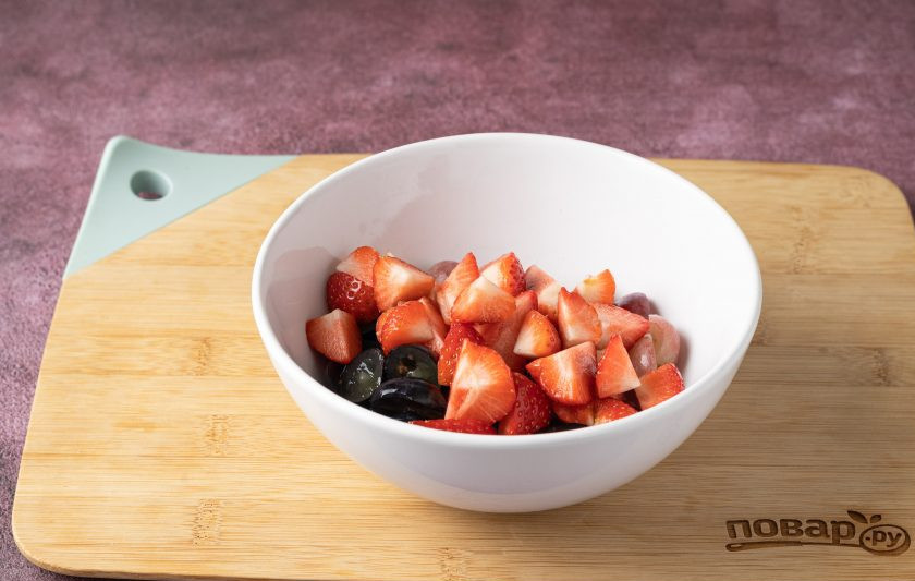 1. Этап. Фруктовый салат с клубникой и виноградом: Клубнику помойте, отрежьте хвостики. Разрежьте на 2-4 части. Добавьте к винограду.