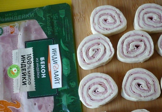 1. Этап. Слоеный пирог с беконом и ветчиной: Рулетики вытащите из морозилки, нарежьте их ломтиками.