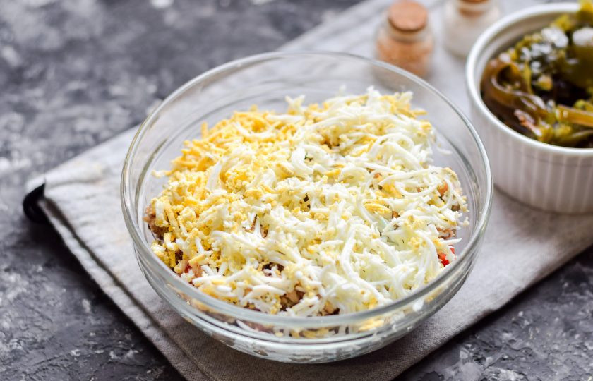 1. Этап. Салат Морское дно с морской капустой: Куриное яйцо сварите вкрутую, очистите от скорлупы, натрите на мелкой терке и выложите поверх консервы.