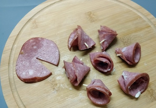 1. Этап. Мини-бутерброды Ассорти: Для 2 бутерброда ломтик копченой колбасы надрезать до середины. Свернуть.