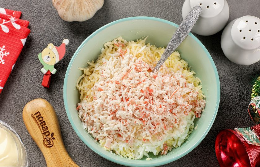 1. Этап. Фаршированные яйца Новогодние драконы: Добавьте тёртый на мелкой тёрке сыр и оставшиеся небольшие кусочки белков. Одну крабовую палочку разверните и отрежьте от неё красную полоску (эту полоску отложите в сторону, она нам потребуется для формирования язычков драконов). Оставшиеся палочки так же натрите на мелкой тёрке.