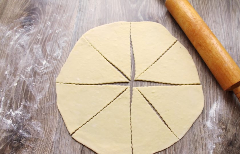 1. Этап. Рогалики с нутеллой: Подошедшее тесто выложите на стол посыпанный мукой и разделите на две части и скатайте в шарики. Накройте и дайте постоять 10 минут. Раскатайте каждый в круг толщиной 0.7 миллиметра и разрежьте на сегменты.