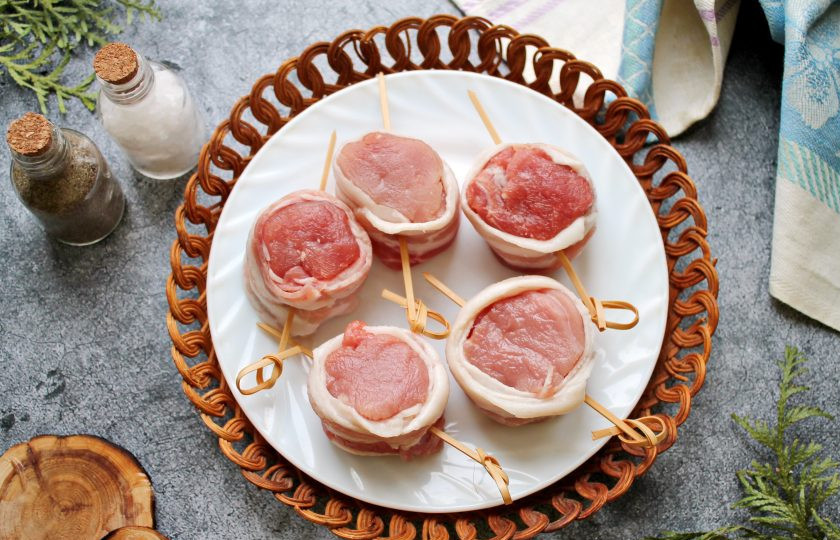 1. Этап. Свиные медальоны в беконе: Вырезку зачистите от пленок и жил, порежьте на кусочки толщиной 3 сантиметра поперек вырезки. Каждый кусочек посолите и поперчите, обверните в полоску бекона и закрепите шпажкой.