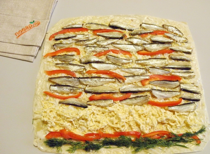 1. Этап. Рулет из лаваша на Новый Год: Отступите от края пару сантиметров и выложите тертый плавленный сыр, его не обязательно тереть, можно порезать брусочками. Порежьте тонкими соломками болгарский перец, распределите по лавашу. Разложите равномерно рыбу. Украсьте зеленью рулет.